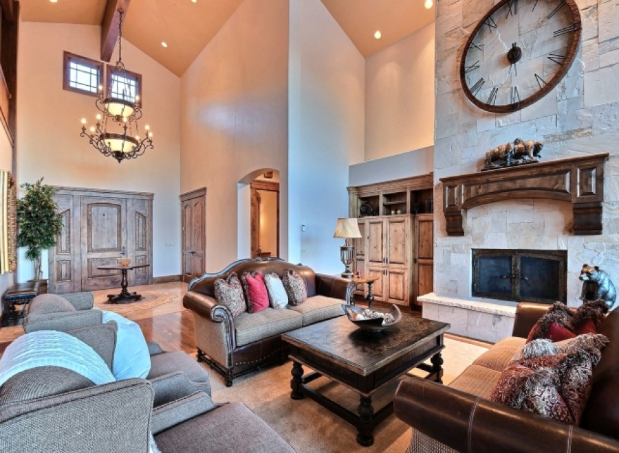 This luxurious living room boasts a stunning stone fireplace with a large clock, high ceilings with a beautiful chandelier, and ample seating for relaxation.