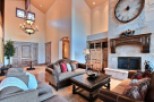 This luxurious living room boasts a stunning stone fireplace with a large clock, high ceilings with a beautiful chandelier, and ample seating for relaxation.