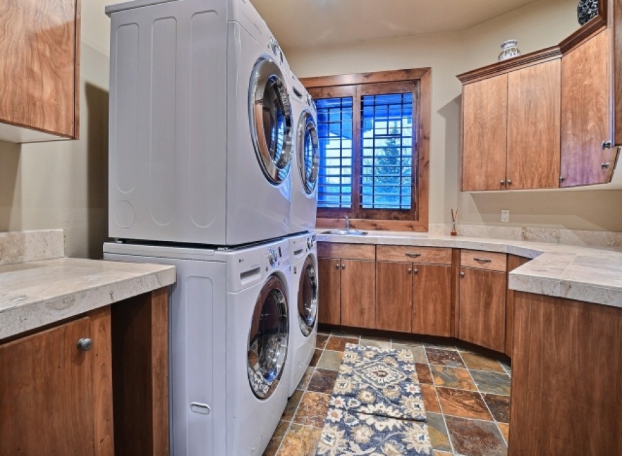 This stunning laundry room boasts a stackable washer and dryer, ample counter space, and rich wood cabinetry.