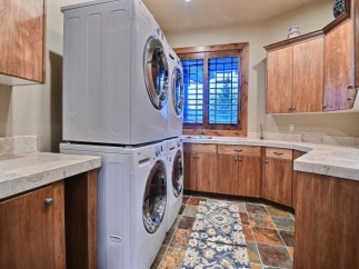 This stunning laundry room boasts a stackable washer and dryer, ample counter space, and rich wood cabinetry.