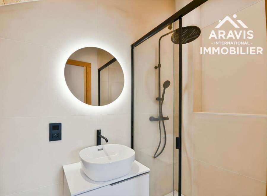 Step into a modern bathroom oasis! This stunning space features a sleek, round illuminated mirror, a stylish sink, and a glass-enclosed shower.