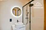 Step into a modern bathroom oasis! This stunning space features a sleek, round illuminated mirror, a stylish sink, and a glass-enclosed shower.