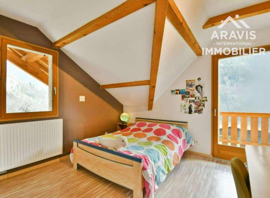 Discover this charming bedroom featuring a cozy bed with a colorful comforter and a unique sloped ceiling with exposed wooden beams.