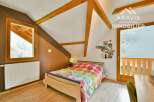Discover this charming bedroom featuring a cozy bed with a colorful comforter and a unique sloped ceiling with exposed wooden beams.