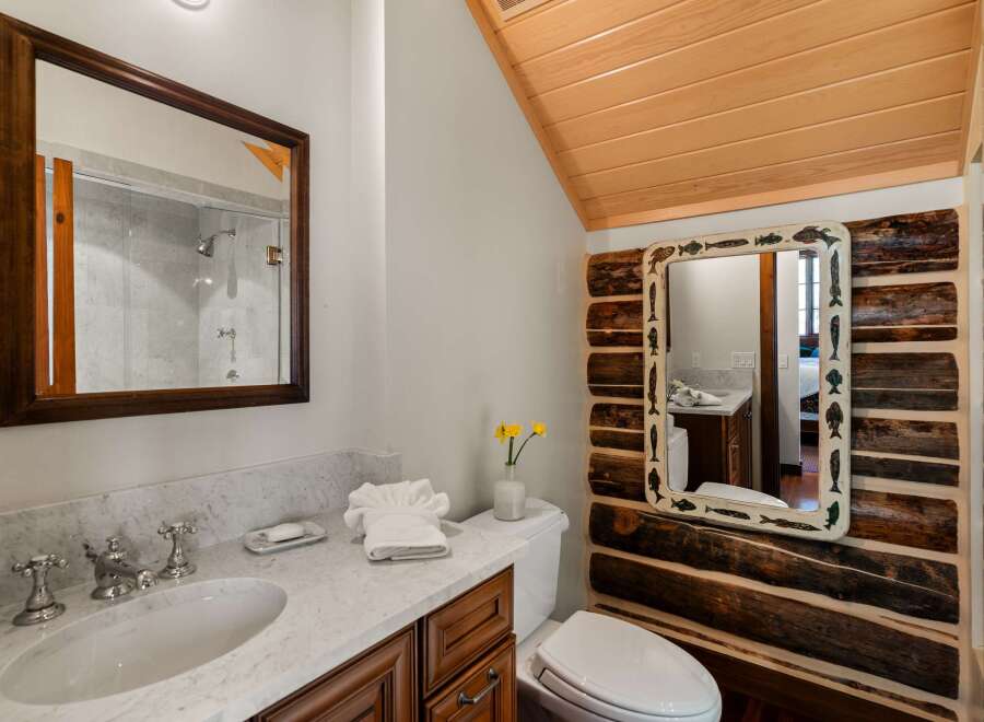 Step into a rustic bathroom retreat, featuring a unique log-cabin style accent wall and a charming fish-themed mirror.