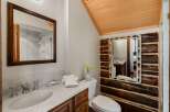 Step into a rustic bathroom retreat, featuring a unique log-cabin style accent wall and a charming fish-themed mirror.