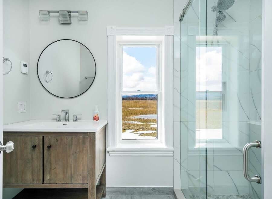 This stunning bathroom features a modern design with a rustic wooden vanity and a sleek, round mirror.