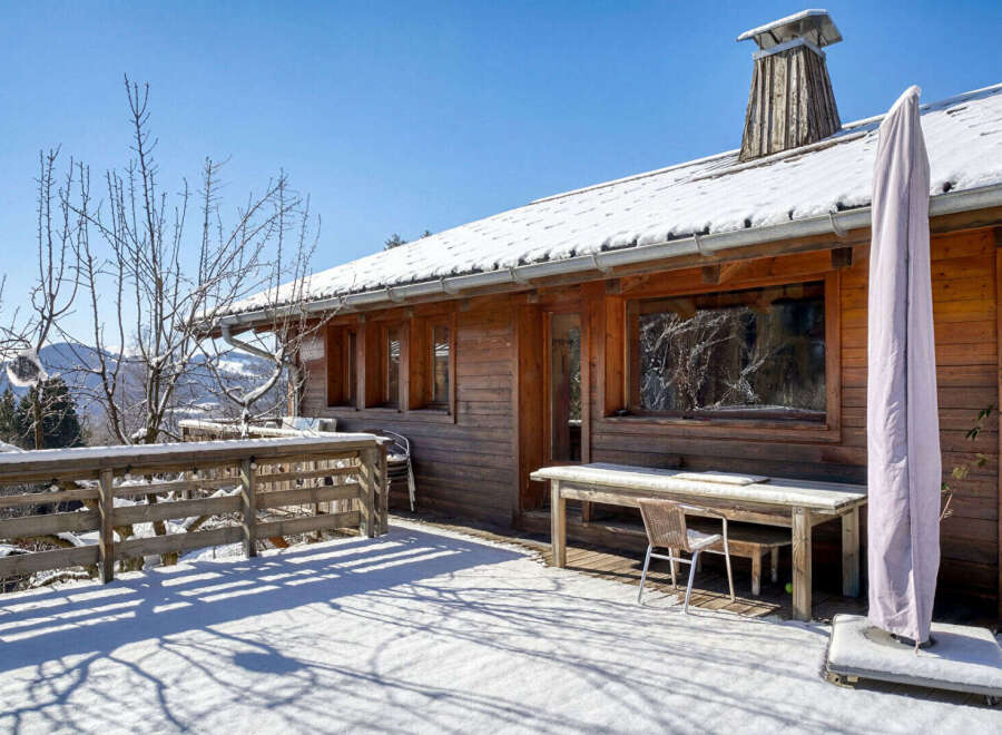 This charming wooden cabin offers a serene escape with its snow-covered surroundings and inviting outdoor space.