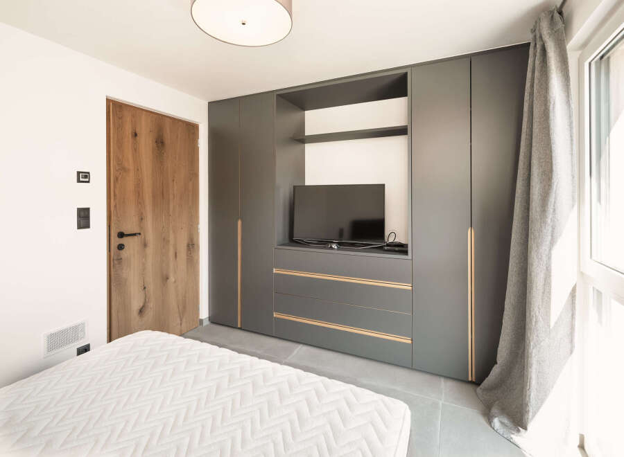 This modern bedroom boasts a sleek, built-in wardrobe with integrated storage and a dedicated TV area, perfect for maximizing space.