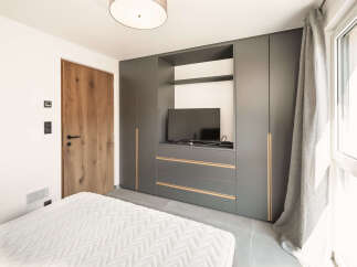 This modern bedroom boasts a sleek, built-in wardrobe with integrated storage and a dedicated TV area, perfect for maximizing space.