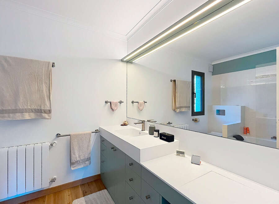 This modern bathroom features a sleek design with a large mirror and integrated lighting, creating a bright and spacious feel.