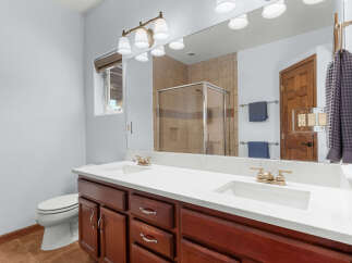 This stunning bathroom features a double vanity with a sleek white countertop and rich wooden cabinetry, offering ample storage and a touch of elegance.