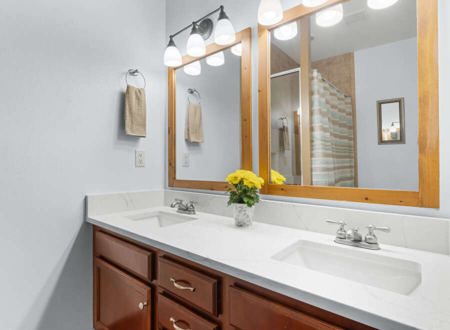 This beautiful bathroom features a double vanity with a bright white countertop and rich wood cabinetry.