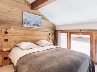 This cozy bedroom features a rustic wooden wall and a comfortable bed, creating a warm and inviting atmosphere.