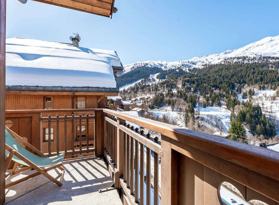 Enjoy breathtaking mountain views from this charming wooden balcony, complete with a comfortable lounge chair perfect for soaking up the sun.