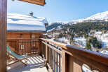 Enjoy breathtaking mountain views from this charming wooden balcony, complete with a comfortable lounge chair perfect for soaking up the sun.
