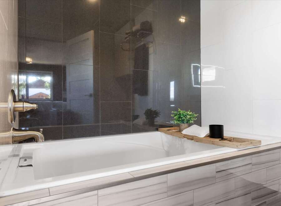 Indulge in the luxury of this modern bathroom, featuring sleek dark tile accents and a pristine white bathtub.