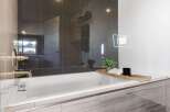 Indulge in the luxury of this modern bathroom, featuring sleek dark tile accents and a pristine white bathtub.