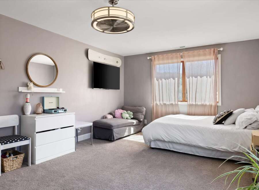 Step into this inviting bedroom, featuring a cozy chaise lounge, a stylish entertainment setup, and a comfortable bed.