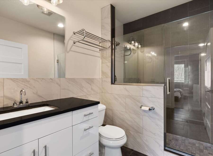 Step into a modern bathroom oasis! This stunning space features a sleek black countertop, a pristine white vanity, and elegant marble-look tiles.