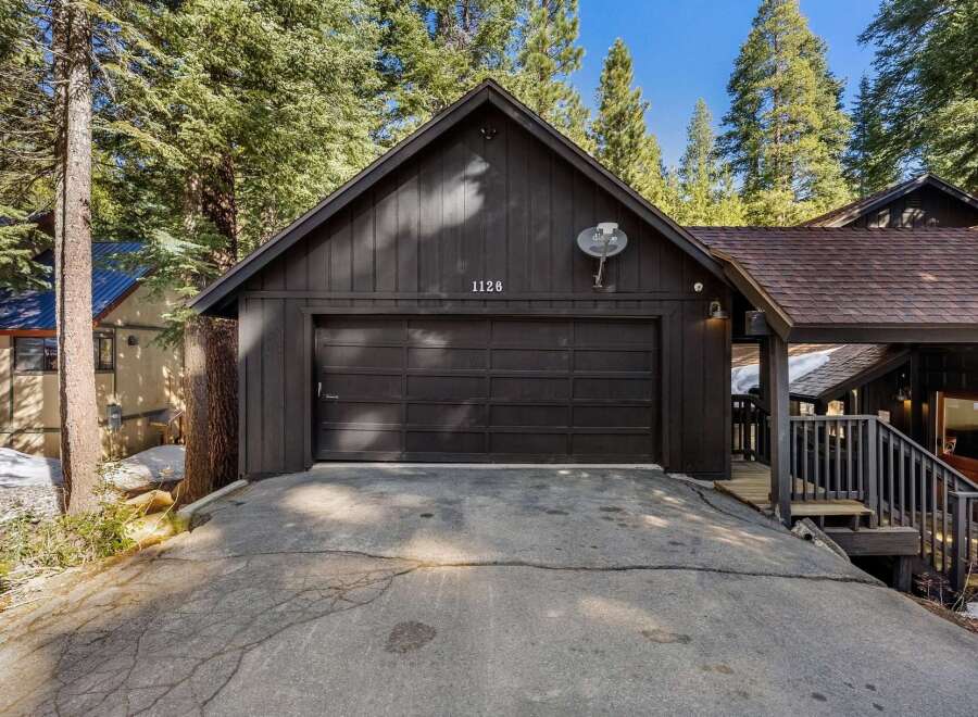 Nestled amidst towering trees, this charming property boasts a striking black exterior and a welcoming garage.