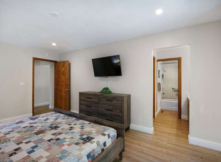 This inviting bedroom features a stylish bed, a mounted TV, and a spacious dresser, offering a comfortable and functional living space.