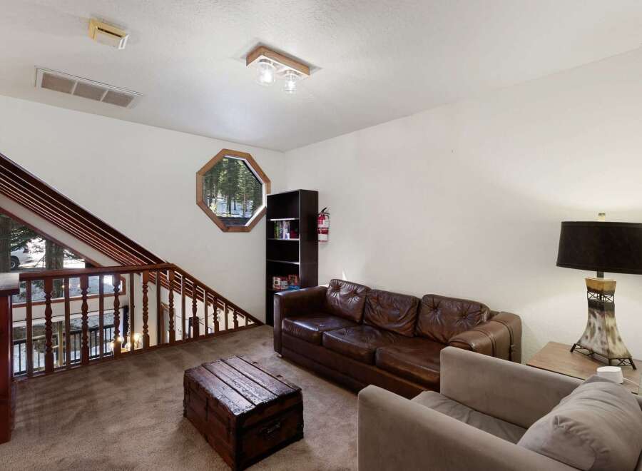 This cozy living space features a unique octagonal window offering scenic views, complemented by a rustic wooden chest and a comfortable leather sofa.
