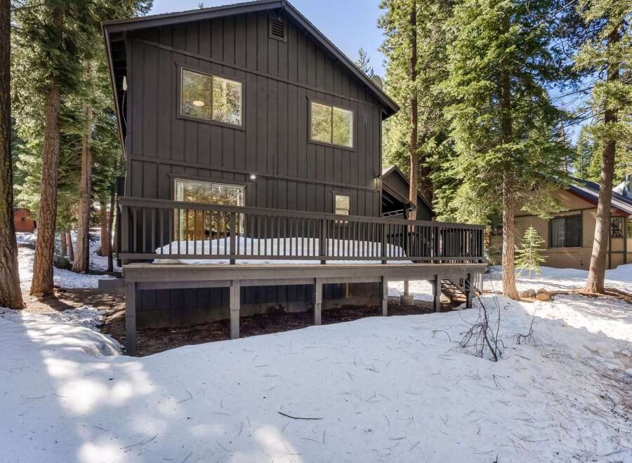 Nestled amidst towering trees, this stunning property boasts a modern aesthetic with its dark exterior and expansive deck.