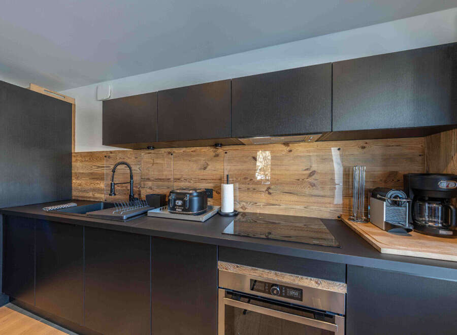 This modern kitchen boasts sleek black cabinetry and a stunning wooden backsplash, creating a stylish and inviting space.