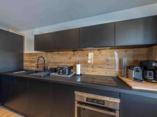This modern kitchen boasts sleek black cabinetry and a stunning wooden backsplash, creating a stylish and inviting space.