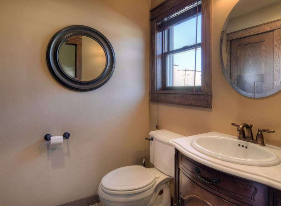 This charming bathroom features a classic design with a round mirror, a wooden vanity, and a toilet.