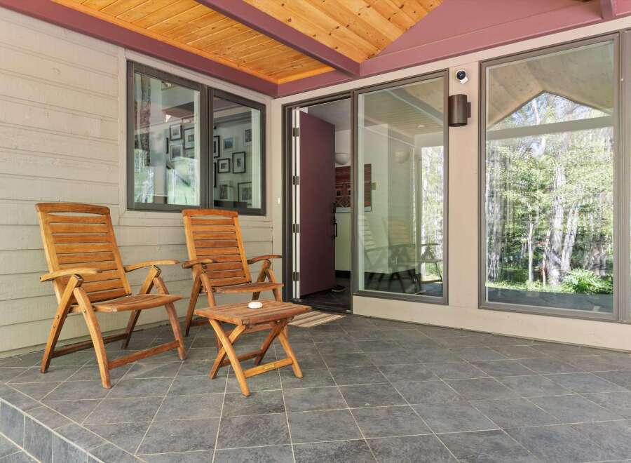 Enjoy the outdoors on this charming covered patio, featuring two wooden Adirondack chairs and a small side table, perfect for morning coffee or evening relaxation.