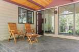 Enjoy the outdoors on this charming covered patio, featuring two wooden Adirondack chairs and a small side table, perfect for morning coffee or evening relaxation.