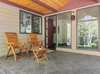Enjoy the outdoors on this charming covered patio, featuring two wooden Adirondack chairs and a small side table, perfect for morning coffee or evening relaxation.