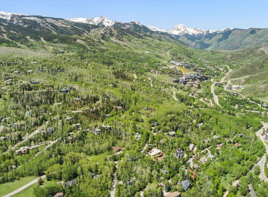 Experience luxury mountain living in this stunning aerial view of a sprawling estate nestled amidst lush greenery and majestic snow-capped peaks.