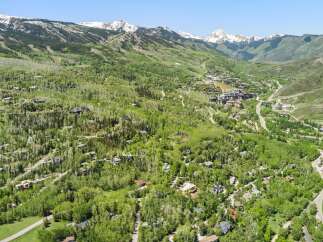 Experience luxury mountain living in this stunning aerial view of a sprawling estate nestled amidst lush greenery and majestic snow-capped peaks.
