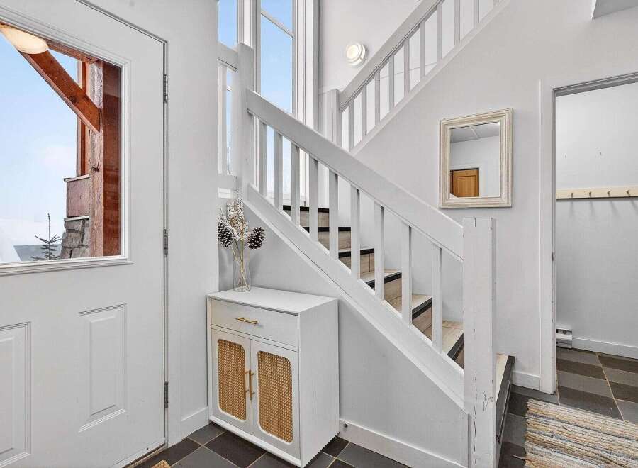 Step into this inviting entryway, showcasing a stylish staircase and a charming white cabinet with woven accents.