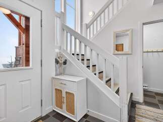 Step into this inviting entryway, showcasing a stylish staircase and a charming white cabinet with woven accents.