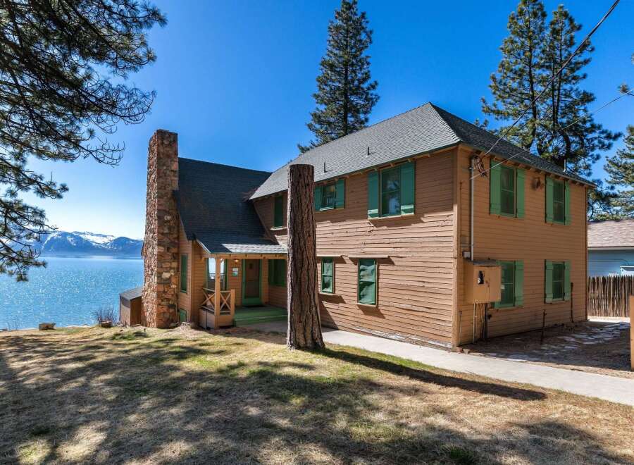 Nestled on the serene waterfront, this charming property boasts a classic design with a rustic stone chimney and inviting green shutters.
