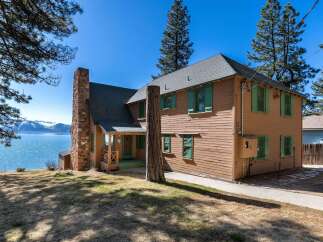 Nestled on the serene waterfront, this charming property boasts a classic design with a rustic stone chimney and inviting green shutters.