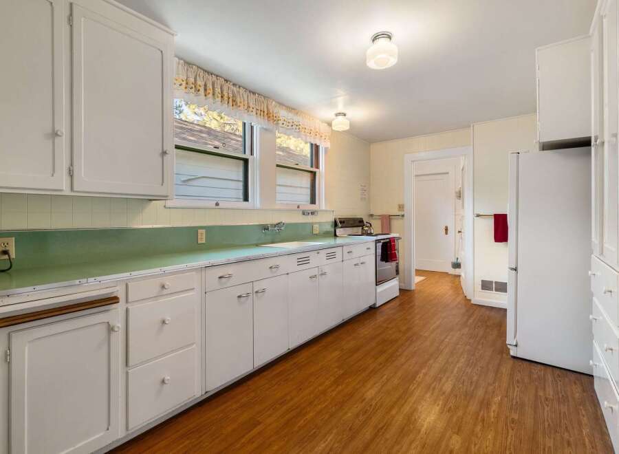 Step back in time with this charming kitchen! Featuring classic white cabinetry, a retro green countertop, and original hardware, this space exudes vintage appeal.