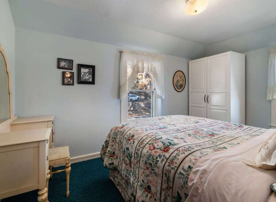 Step into this charming bedroom, featuring a cozy bed adorned with a floral quilt and a serene ambiance.