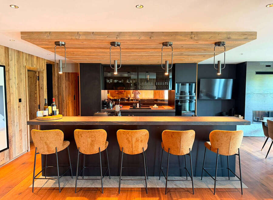 Experience modern luxury in this stunning kitchen featuring a sleek dark island with comfortable bar stools and a warm wooden ceiling.