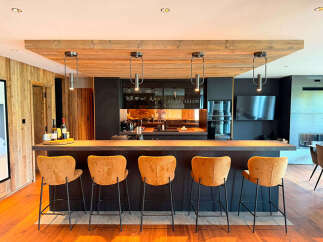 Experience modern luxury in this stunning kitchen featuring a sleek dark island with comfortable bar stools and a warm wooden ceiling.