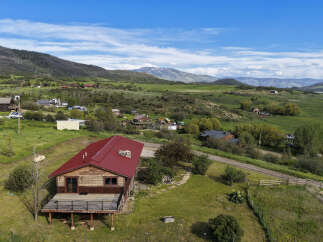 Experience serene mountain living in this charming log home, featuring a durable red metal roof and a spacious wooden deck perfect for enjoying the breathtaking panoramic views.