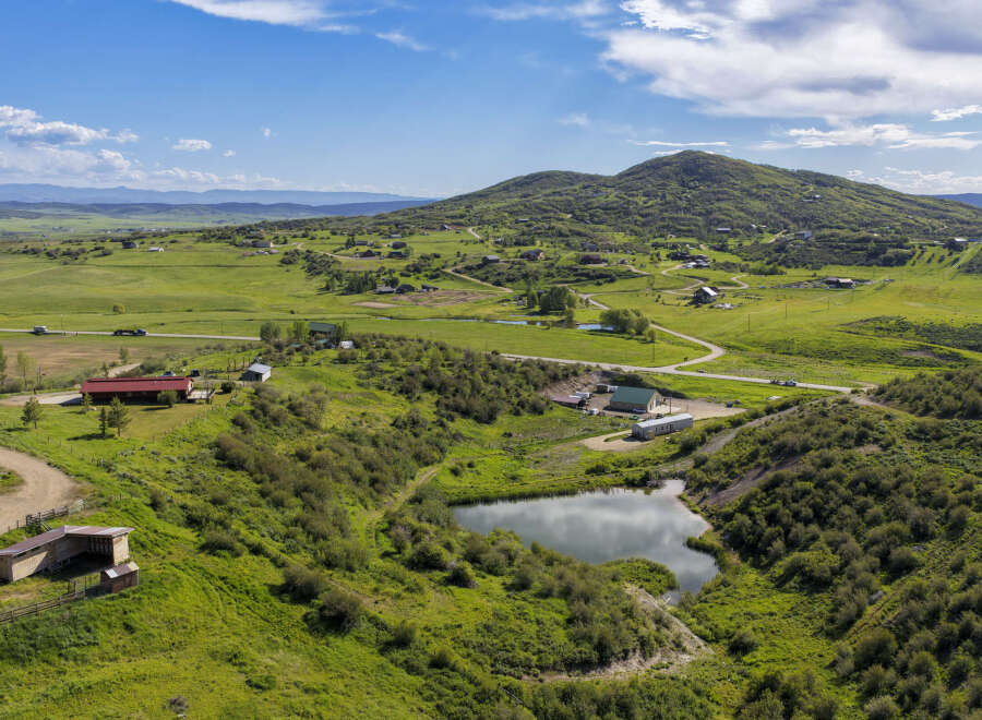 Discover this expansive rural property featuring a serene pond, multiple outbuildings, and a charming red-roofed home.