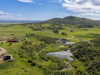 Discover this expansive rural property featuring a serene pond, multiple outbuildings, and a charming red-roofed home.