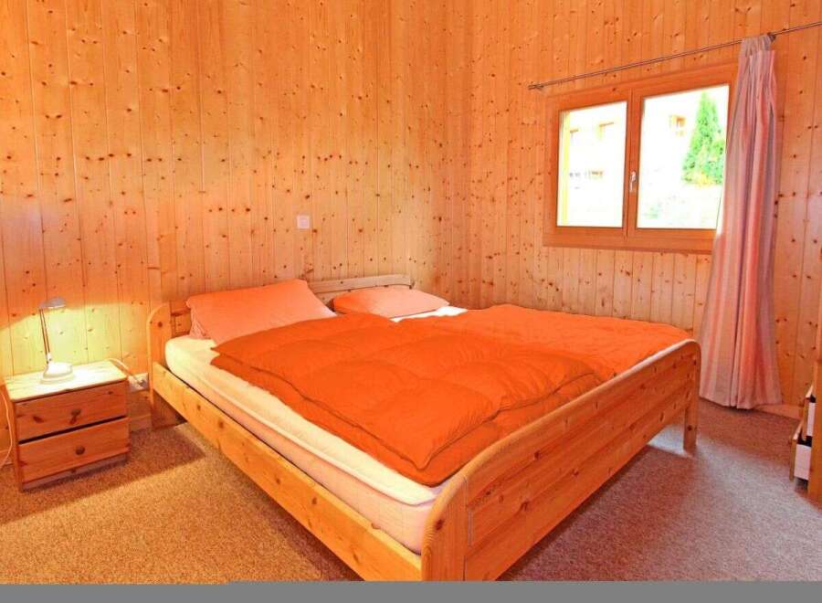This cozy bedroom features warm wooden paneling and a comfortable bed with an inviting orange comforter.