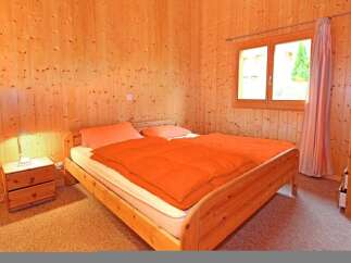 This cozy bedroom features warm wooden paneling and a comfortable bed with an inviting orange comforter.