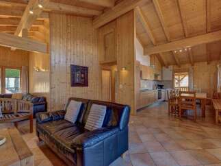 Experience rustic charm in this spacious wooden chalet, featuring a cozy living area with a leather sofa and a well-equipped open-plan kitchen and dining space.